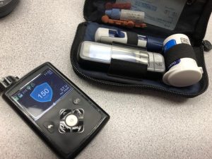 Pictured above is a glucose monitor, or meter, as well as an insulin pump showing a blue shield with a blood sugar on it. 